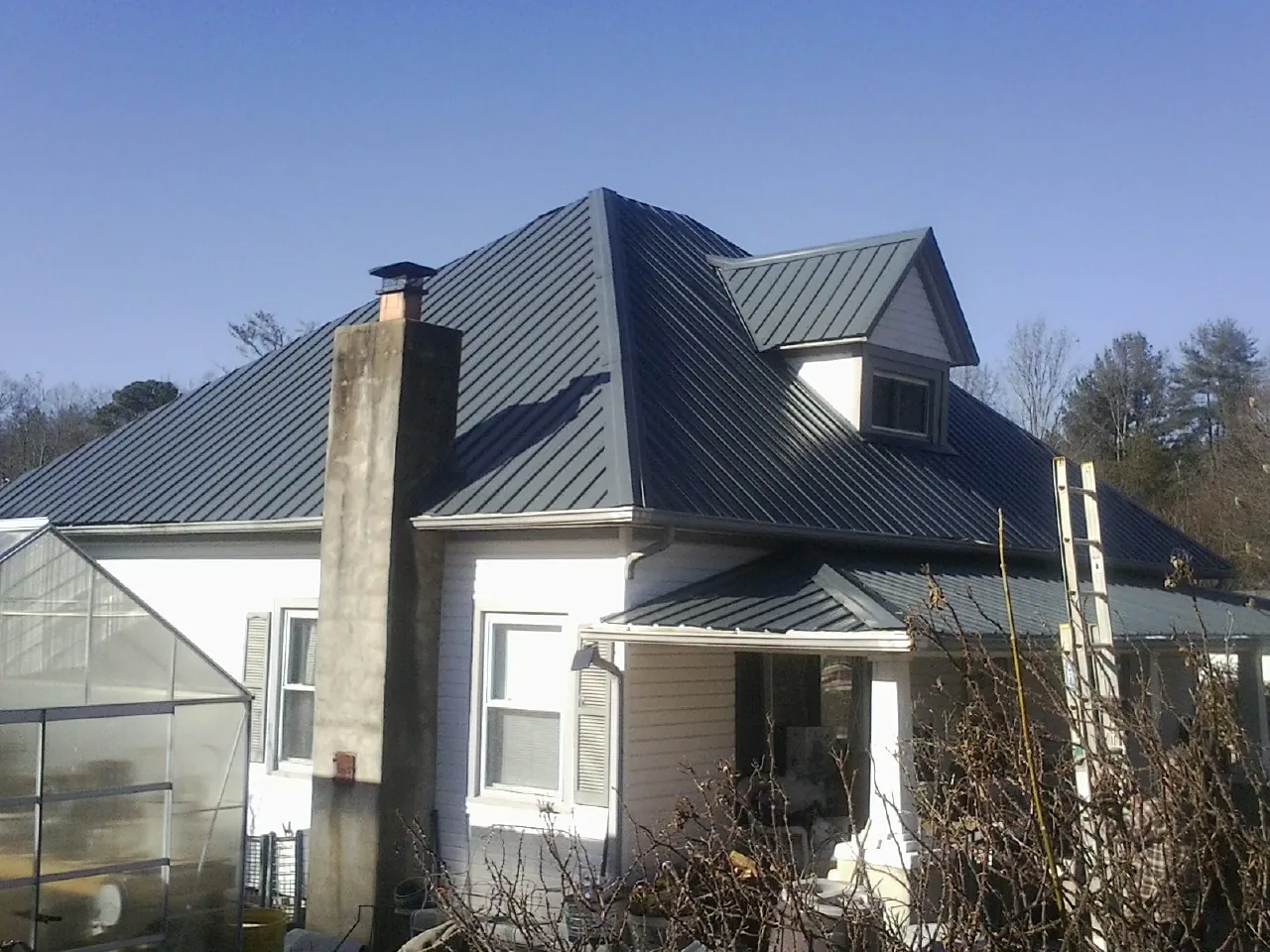 Dark blue standing seam metal roof on a white farmhouse with dormer — Slate & Tile Roof Repair by Roofing Brothers in Riner