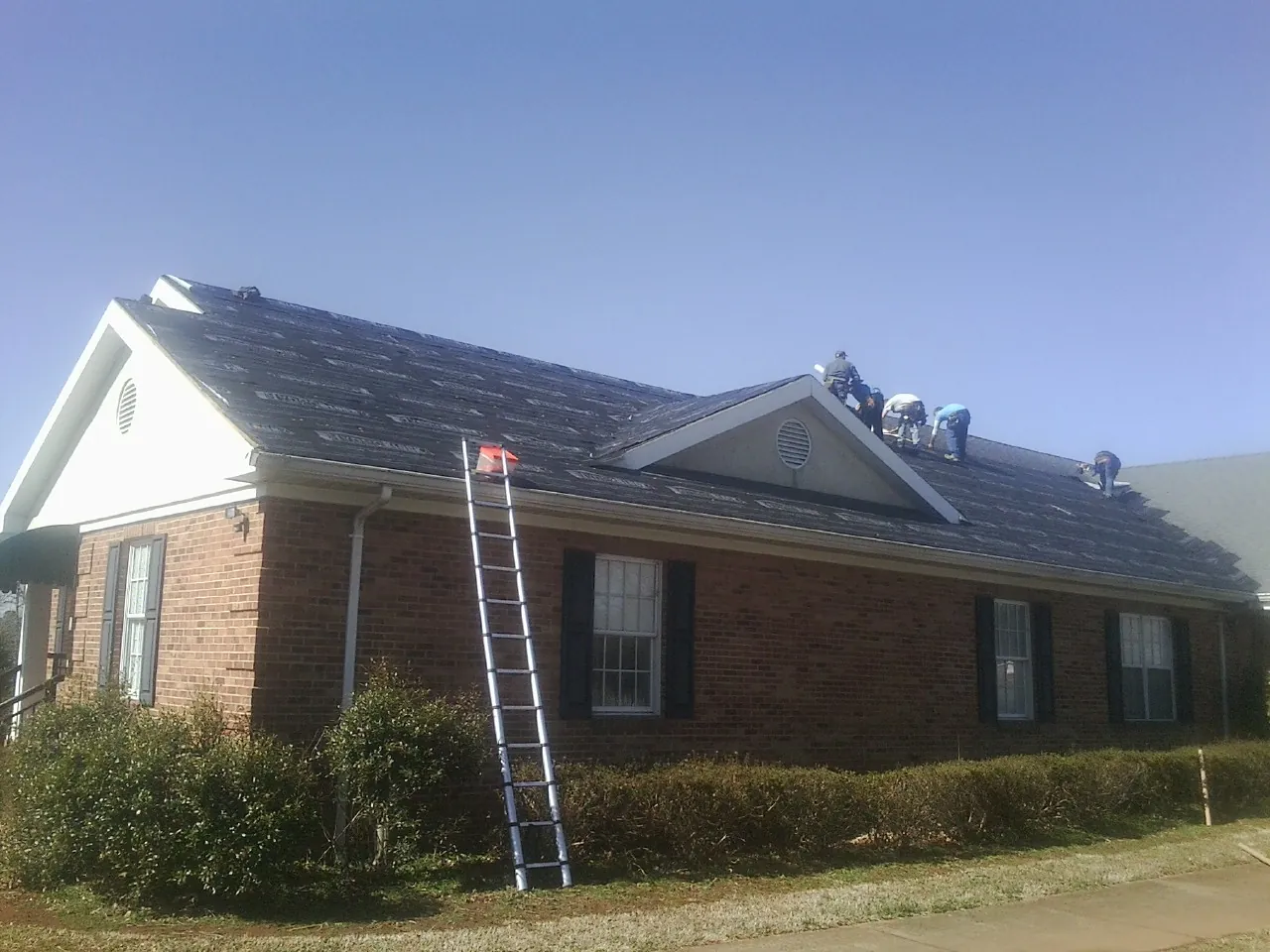 Crew tearing shingles off a brick ranch roof with a ladder set — Emergency Roof Repair work by our crew in Riner