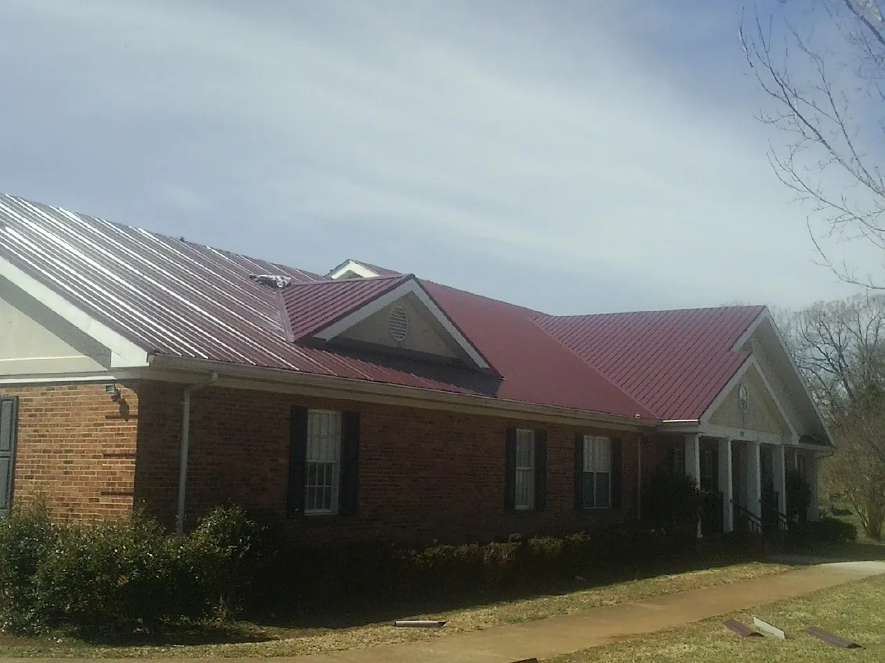 Red metal roof with gabled entries on a long brick building, from a Hail Damage Roof Repair job in Riner