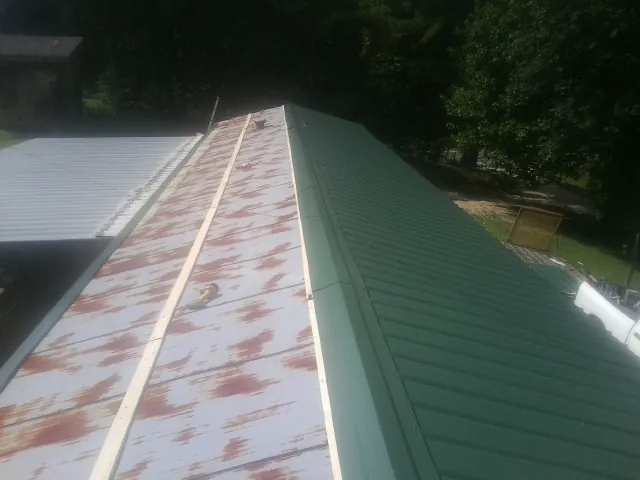 Old rusted panels beside newly installed green metal roofing — Wind Damage Roof Repair by Roofing Brothers in Riner
