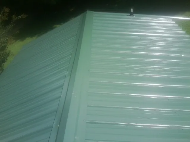 New green metal panels meeting at the ridge of a roof — Flat Roof Repair work by our crew in Riner