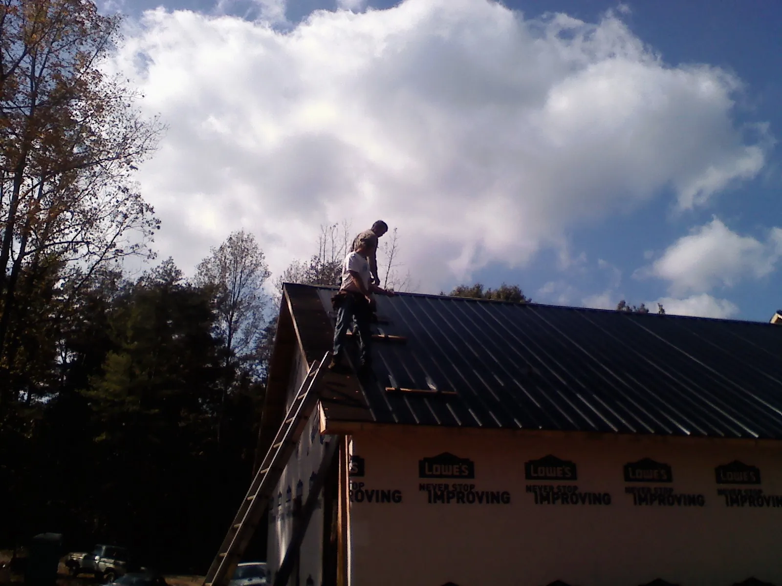 Roofer fastening dark metal panels high against a cloudy sky, from a Roof Inspection job in Riner