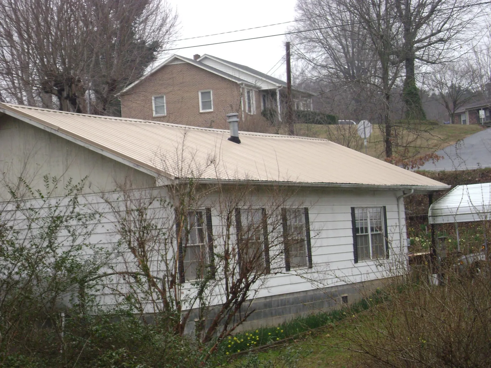 Tan metal roof on a white sided house set into a hillside — Commercial Roofing by Roofing Brothers in Riner